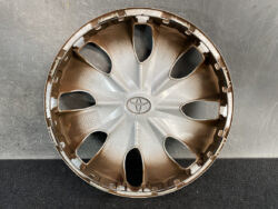 Toyota hubcap with eight-spoke design and central emblem lying on a dark surface