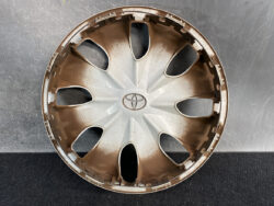 Brown plastic Toyota hubcap with eight teardrop spokes and centered logo, lying on a dark workbench.