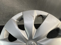 Close-up of a silver car wheel hubcap with scratches and a chipped area near a vent/opening.