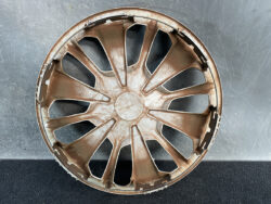 Brown plastic car wheel hubcap with 12 spokes, dusty and scratched, lying on a gray surface