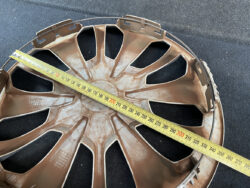 Brown alloy car wheel rim with multiple spokes, viewed on a dark surface, a tape measure laid diagonally across it showing about 30 cm to 31 cm.