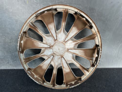 Dusty brown plastic car wheel hubcap with many spokes, laid flat on a dark surface.