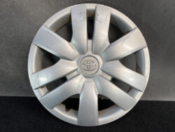 Silver Toyota hubcap with the emblem in the center and several surface scratches cast across the spokes.