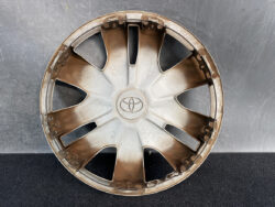 Dusty Toyota hubcap/wheel cover with eight spokes and center emblem, viewed head-on.