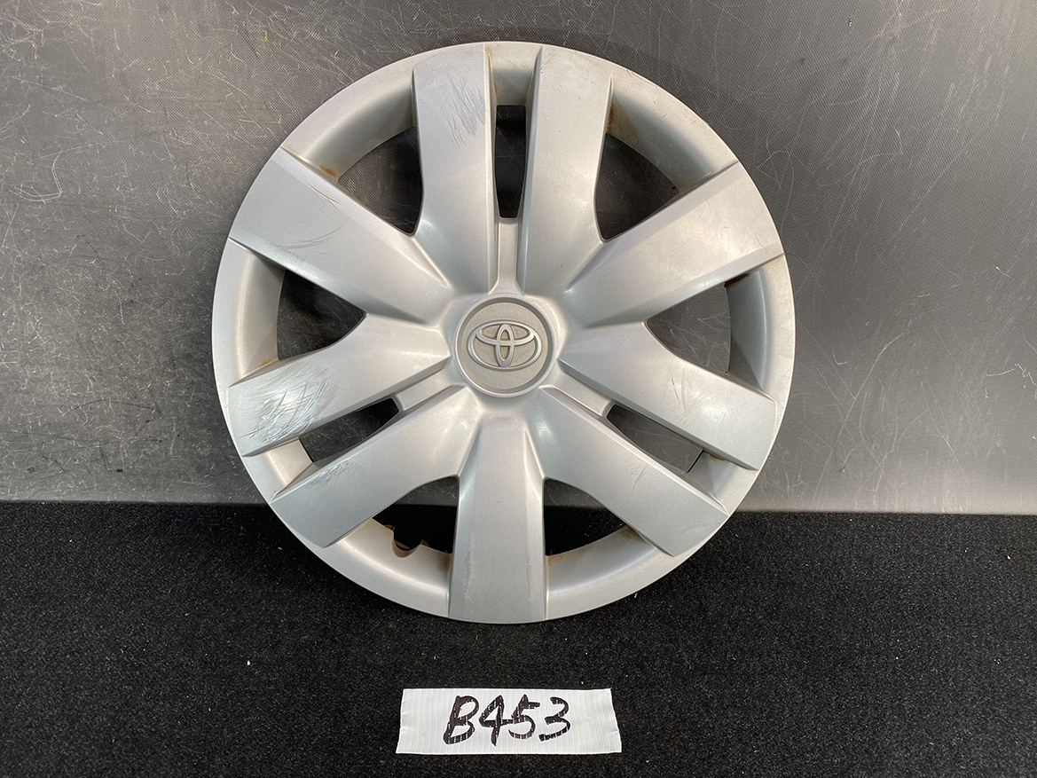 B453_1 TOYOTA BELTA SCP92 NCP96 KSP92 Genuine 14inch WHEEL CAP / HUB CAP x1 » NZ.95 » JDM-PARTS NZ » JDM-PARTS NZ Silver Toyota hubcap with an eight-spoke star design, showing light scratches, resting on a dark surface with a small handwritten tag labeled B453 TOYOTA BELTA SCP92 NCP96 KSP92 Genuine 14inch WHEEL CAP / HUB CAP x1 » JDM-PARTS NZ