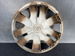 Dusty silver Toyota hubcap with eight spokes, placed against a dark surface.