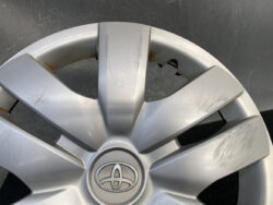 Close-up of a silver Toyota wheel hubcap with visible scratches and small rust spots near the spokes and center emblem.