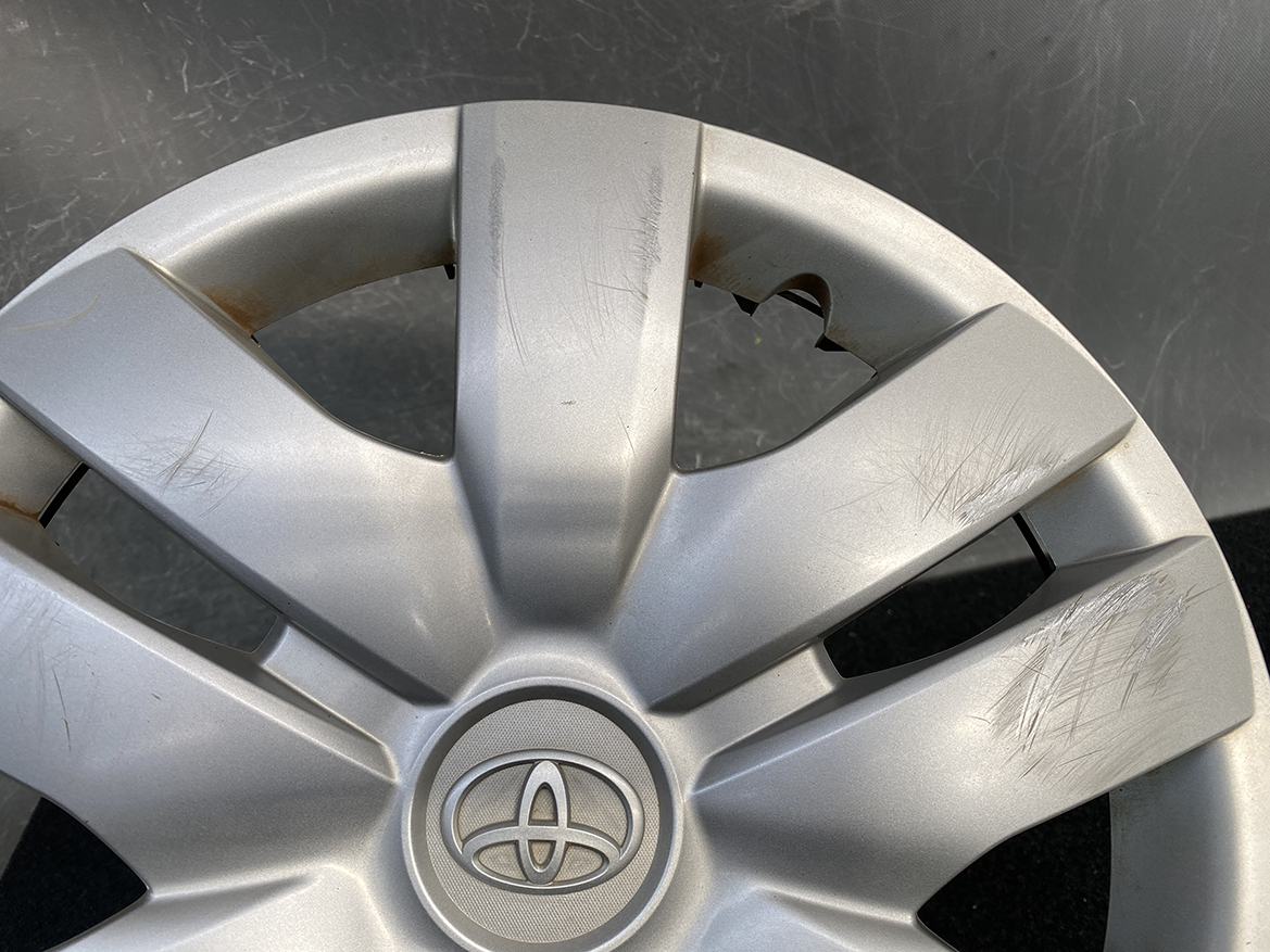 B453_4 TOYOTA BELTA SCP92 NCP96 KSP92 Genuine 14inch WHEEL CAP / HUB CAP x1 » NZ.95 » JDM-PARTS NZ » JDM-PARTS NZ Close-up of a silver Toyota wheel hubcap with visible scratches and small rust spots near the spokes and center emblem. TOYOTA BELTA SCP92 NCP96 KSP92 Genuine 14inch WHEEL CAP / HUB CAP x1 » JDM-PARTS NZ