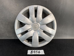 Silver Toyota hubcap with multiple scratch marks, lying on a dark surface with a B454 label nearby.