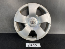 Silver Toyota hubcap with the emblem at center, propped against a dark backdrop; a small label reads B455 nearby.