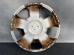 Rusty metal car wheel hubcap with five spokes resting against a dark wall surface