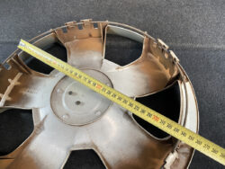 Circular metal impeller/fan wheel with multiple blades and a yellow measuring tape laid diagonally across it for scale.