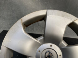 Close-up of a silver Toyota hubcap with multiple scuffs and scratches on the spokes edge.