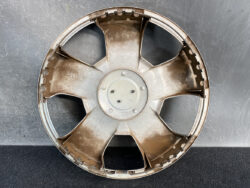 Rusty circular car wheel rim with six thick spokes, shown front-on against a gray background.