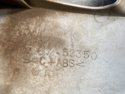 Close-up of embossed codes on a part: '42062 = 52350', 'PC+ABS', with surrounding symbols on a dusty surface.
