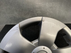 Close-up of a silver car wheel cover with visible surface scratches and scuffs on a dark background.
