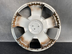 Round metal wheel hubcap with five spokes and rust stains on a dark surface