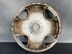 Interior of a dusty car wheel hubcap with four openings and central mounting nub visible, resting on a dark surface