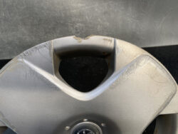 Gray plastic wheel hubcap with deep scratches and a chipped top edge, from vehicle use