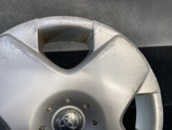 Close-up of a silver Toyota hubcap with scratches and scuffs, center emblem visible