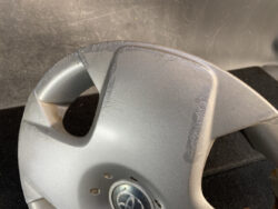 Close-up of a car steering wheel center with a scratched, worn outer edge on a silver rim; Toyota emblem visible at the center.