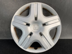Silver Honda hubcap with central emblem and five spokes, showings rust around inner rim and minor scuffs on surface.