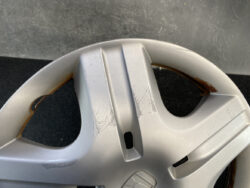 Close-up of a silver alloy wheel with curb rash and scratches along the rim, showing rust along the inner edge.