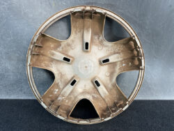 Rusty beige six-spoke wheel hubcap with dirt, placed on a dark surface and showing a Honda stamp in the center area.