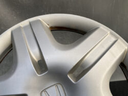 Close-up of a silver Honda wheel hubcap with scuffs and a rusted rim visible around the edge.