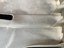 Close-up of a gray molded Honda plastic part with embossed text: HONDA, PP-GF20, and part number 44733-SAA-N010-M1; visible circular mold marks and seams.
