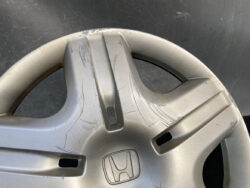 Close-up of a silver Honda hubcap with multiple deep scratches and scuffs, showing damage to the wheel cover.