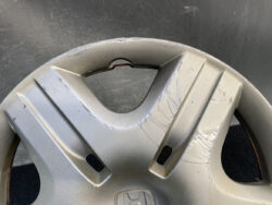 Close-up of a silver plastic car wheel cover with visible scratches and a cracked center area.