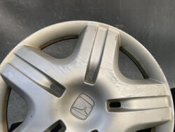 Honda wheel cover with a scratched, scuffed silver surface and centered logo