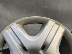 Close-up of a silver car wheel hubcap with visible scratches and scuffs, featuring a triangular center opening and vent-like cutouts on the spokes.