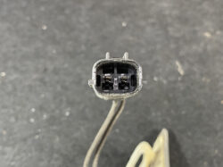 Close-up of a small oval 2-pin electrical connector with two metal pins inside, likely automotive or sensor plug, held by a cable