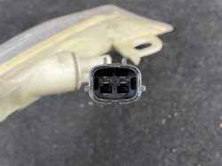 Close-up of an oval two-pin automotive electrical connector seen from the front with side latch tabs still visible.