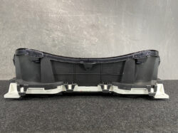 Rear view of a curved car dashboard instrument cluster housing with a clear lens and mounting brackets on a textured surface.