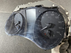 Damaged car instrument cluster with a cracked lens, showing speedometer up to 180 km/h and a tachometer on the left.