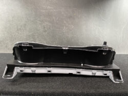 Automotive instrument cluster housing with a clear plastic cover and mounting brackets on a black base.