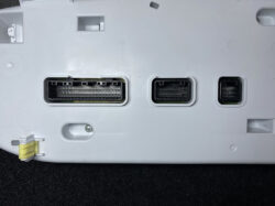 Back panel of a white electronic device with three multi-pin connectors (large, medium, small) and a yellow latch at the lower-left.
