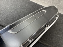 Close-up of a glossy black car center console with a recessed rectangular panel under a clear protective cover; fastened by screws.