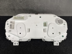 Rear view of a Subaru instrument cluster module in white plastic, with multiple connectors and mounting points visible on a workshop surface.