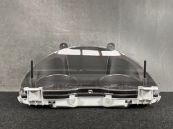 Car instrument cluster with speedometer and tachometer behind a clear curved cover and mounting brackets far end.