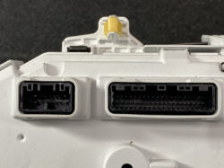 Close-up of a white automotive control module with two large black multi-pin connectors and a yellow latch on top.