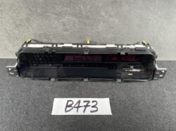 Rear-facing view of a car digital instrument cluster module with two red LED displays and mounting brackets on a dark work surface, tag 'B473' in front.