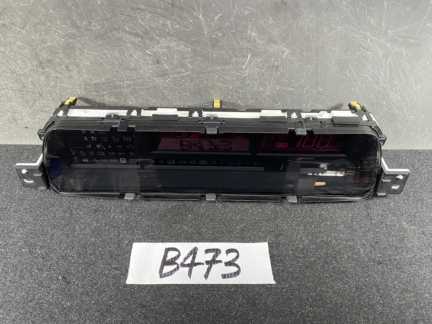 B473_2 TOYOTA PRIUS C AQUA NHP10 Genuine Instrument Cluster 83800-5CU90 » NZ1.95 » JDM-PARTS NZ » JDM-PARTS NZ Rear-facing view of a car digital instrument cluster module with two red LED displays and mounting brackets on a dark work surface, tag 'B473' in front. TOYOTA PRIUS C AQUA NHP10 Genuine Instrument Cluster 83800-5CU90 » JDM-PARTS NZ