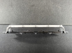 Long black automotive electronic module with multiple plastic clips, resting on a dark textured surface (likely a vehicle control unit).