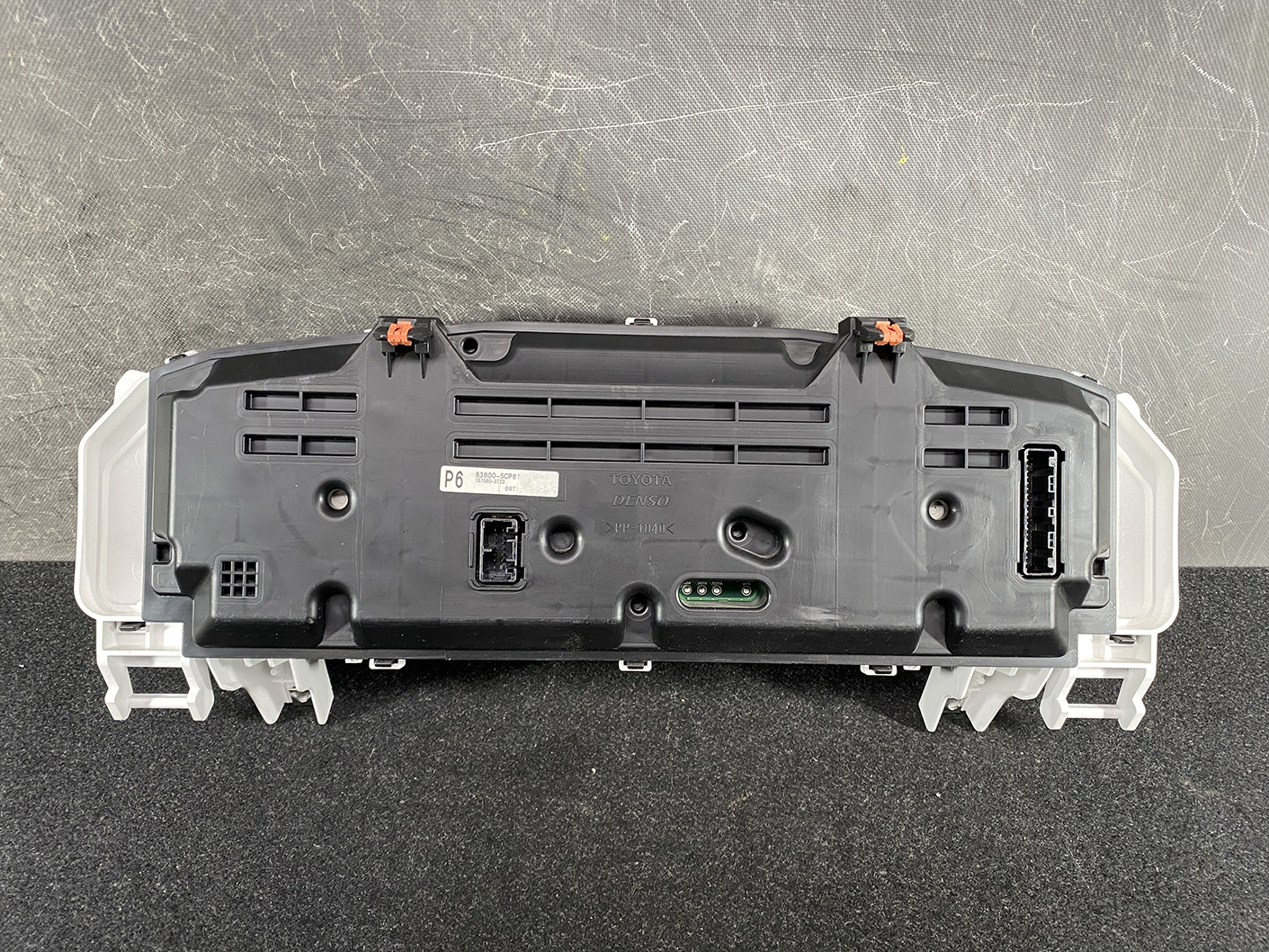B474_7 TOYOTA SIENTA NHP170 Genuine Instrument Cluster 83800-5CP61 » NZ1.95 » JDM-PARTS NZ » JDM-PARTS NZ Rear view of a Toyota instrument cluster module with connectors, orange clips, and mounting brackets TOYOTA SIENTA NHP170 Genuine Instrument Cluster 83800-5CP61 » JDM-PARTS NZ