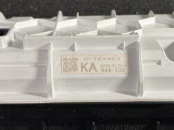 Close-up of a white plastic automotive component with a beige label showing a QR code, 'KA', and the number 944-130.