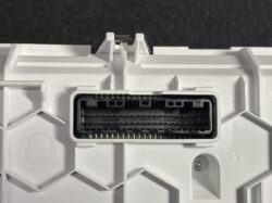 Close-up of a rectangular multi-pin electrical connector on a white plastic module (likely automotive control unit).